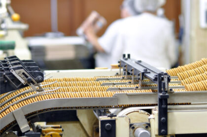 Industrial cookie line with hundreds of cookies on a conveyor belt in a modern factory, with employees faintly visible in the background.