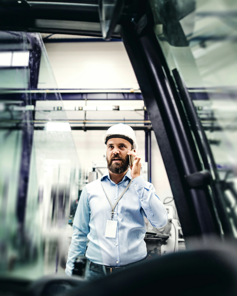 Technical advisor wearing a helmet making a phone call in a factory hall about energy savings through heat recovery.