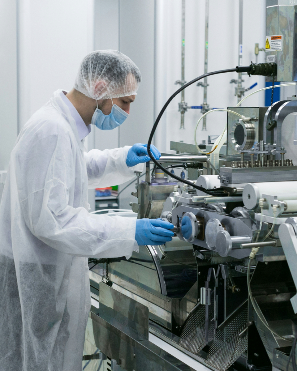 Technician in protective clothing working on an industrial machine in a sterile production environment.