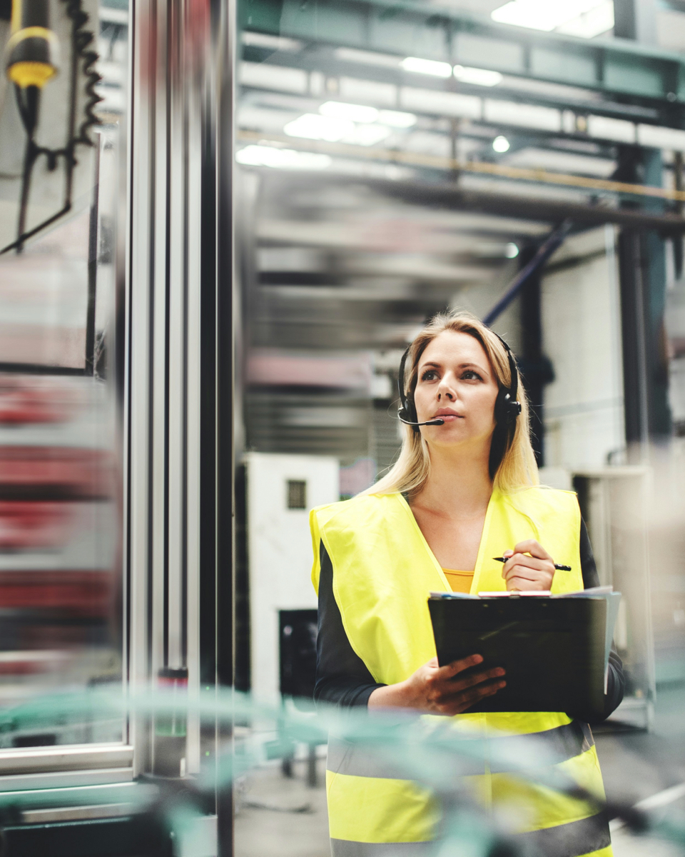 Female technician in safety vest with headset conducting an inspection in an industrial environment for heat recovery.