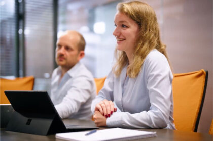 Twee collega’s in gesprek tijdens een zakelijke vergadering, met een vrouwelijke medewerker op de voorgrond die lacht en luistert.