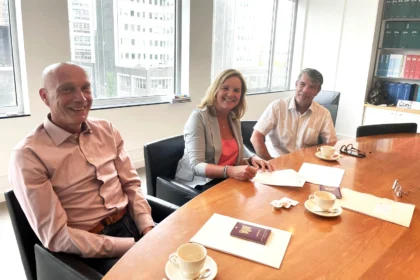 Martine Goedegebuure signs the acquisition of Heat Matrix by Bos Nieuwerkerk alongside two men at a conference table with a view of the city.